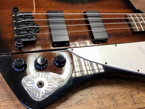 This image shows a close-up of a unique electric guitar featuring a wooden body with a glossy finish. It includes a bridge with multiple strings, two pickups, and a control plate with knobs for adjusting tone and volume. The design elements include a 825 silver and 585 gold detail.