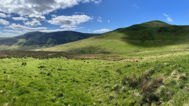 Gentle contours of the Pentland Hills with a mostly blue sky, some clouds casting a shadow on one of the hills