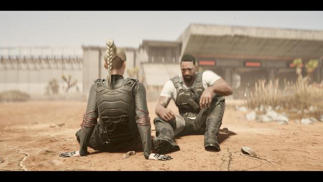 A man and a woman sit in a desolate, sandy environment. The woman, with a braided hairstyle, wears a black tactical outfit, while the man is in a white shirt and tactical gear. They appear to be engaged in a serious conversation.