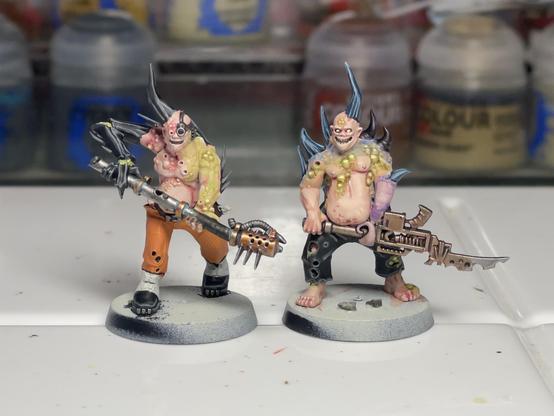 Two mostly finished Poxwalkers. One with insect arm and orange pants holding a flamer weapon, and the other with protruding blue spikes and some kind of blade