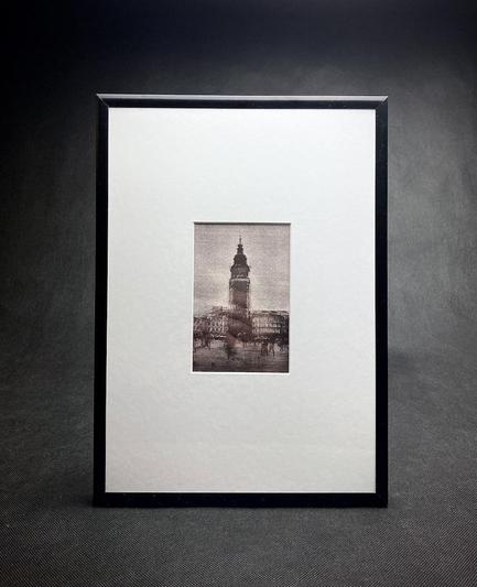 Argyrotype print showing Kraków's Town Hall on the Main Square, bathed in a dreamlike blur. The multi-exposure layers the scene in a delicate tremor, as if time itself wavers. Shadows of passers-by stretch and merge on the pavement, fleeting silhouettes that resemble wandering ghosts, drifting through time. Print is presented in a thin black aluminium frame and white passe partout.