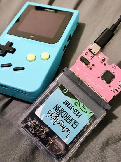 An image of a blue Modretro Chromatic and a GBxCart RW 1.4c (pink PCB) that has a copy of Winsley's Guardian inserted into it (clear cartridge).