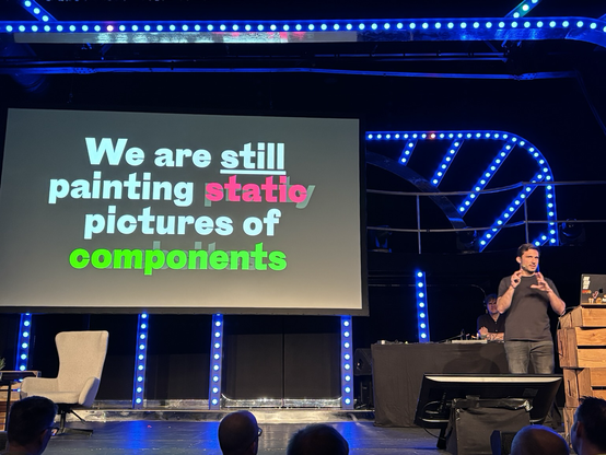 Matthias Ott on stage, screen projector shows slide with the content “We are still painting static pictures of components”. 