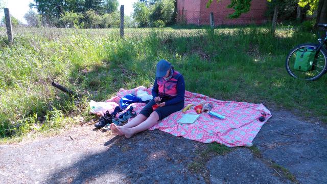 Frau sitz auf großer Pausendeckel am Uferbereich der Havel
 Um die herum die Verpflegung für die Pause