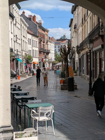 a quiet, curved, pedestrianized street with retail, restaurants, and residences, with people walking and standing calmly