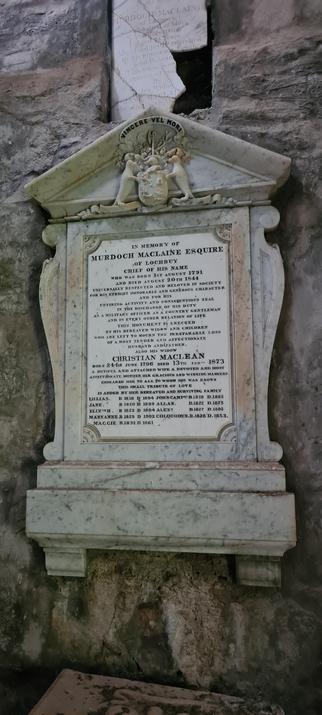 An ornate marble gravestone in a mausoleum. It has a coat of arms, supported by cute seals, at the top, and the details of the life of Murdoch Maclaine Esquire and his wife, Christian MacLean (sic). The words are ridiculously over the top, with Murdoch apparently “universally respected and beloved in society”.