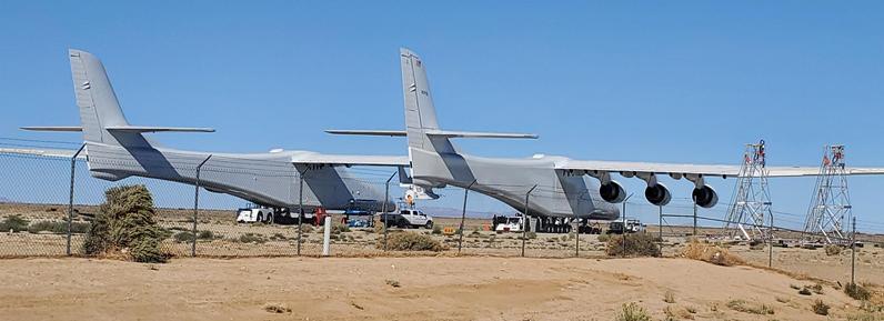 2022 photo, copyright J. Steven York, taken at Mojave Air & Space Port in California. It shows a rearward video of the huge Stratolaunch carrier aircraft (informally known as the Roc) with an earlier version of the Talon hypersonic research vehicle hanging tiny under the center wing. There are two identical fuselages each with their own rudder and horizontal stabilizer. They are connected by the 385 foot span wing, with three engines, taken from Boeing 747.