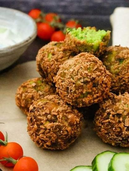 A pile of crispy falafel next to a yoghurt dip & cherry tomatoes