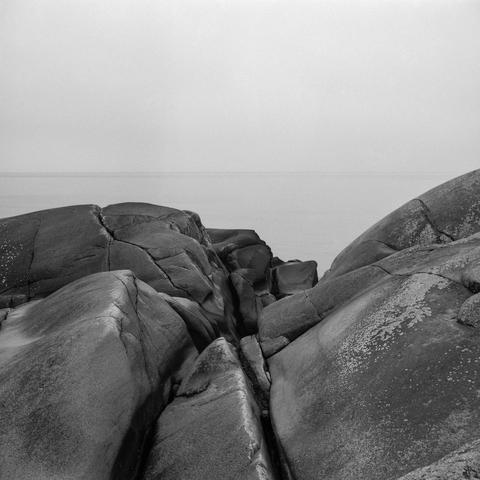 Wavy rock formations with lots of cracks on the shore. Foggy, calm seas in the background. The horizon is barely visible.