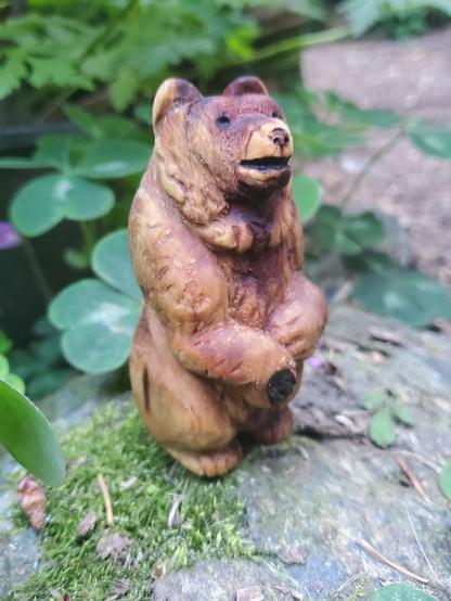 the bear carving facing right. it is sitting upright on its haunches with one paw raised a little higher than the other