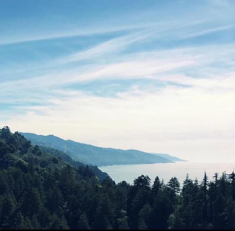 A square picture of a wispy cloudy sky, mountains and trees, and the Pacific Ocean.
