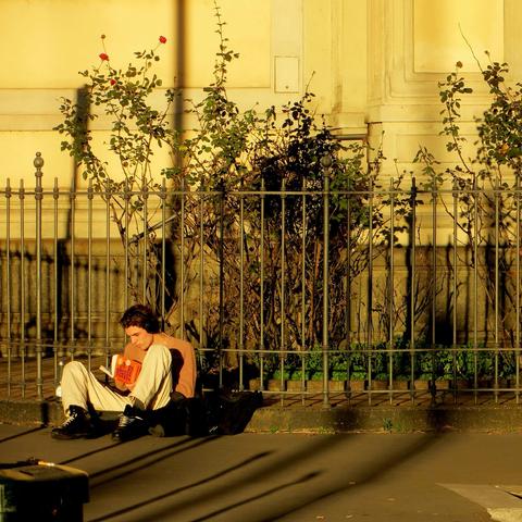 Detail of the person sitting sitting in the lower left corner in the other picture. He is sitting on the walkway and reading a book.