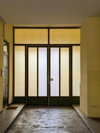 Milchglastüren in weiss und gelb in gelb gestrichenem Durchgang mit schwarzen Rahmen und Messingumrahmung