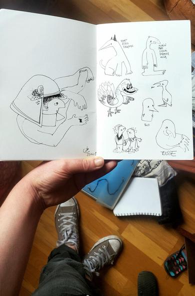 Photo d'une main qui tient un carnet de dessin au-dessus d'un plancher en bordel. Sur le carnet, daté de 2018, un type avec un casque bizarre allongé par terre et qui regarde un tout petit oiseau dans sa main. Un chat-dino bizarre, un oiseau moche qui dit "putain bah j'en ai marre voilà", un dindon vraiment laid, un oiseau avec la mention "rot" un autre "poils", un autre "tousse", et un couple de créatures qui se tient par la main.