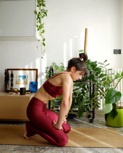 Norayogini performing an abdominal lock, in a living room full of house plants.