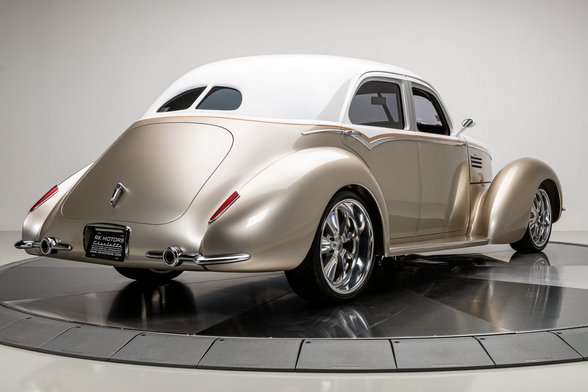 a car, seen from behind in a three quarter view, it has a white roof and gold body, it is vey rounded and graceful looking, large wheel wells 