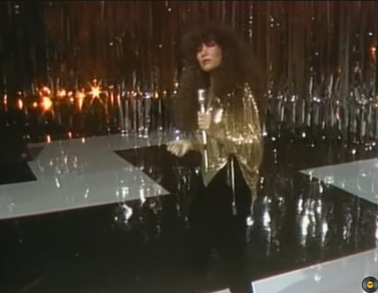 Amanda Miguel on stage with glittery curtains in the background