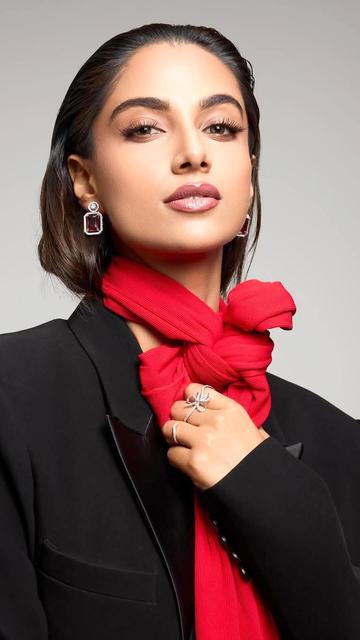 Embracing bold colours and structured silhouettes, Meenakshi Chaudhary pairs a black blazer with red leggings, enhanced by a voluminous red scarf and delicate accessories. Her sleek hairstyle and nude makeup complete this powerful look.