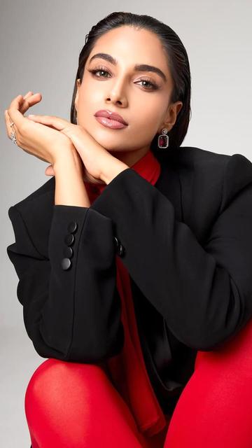 Meenakshi Chaudhary's recent outfit features a tailored black blazer and bold red leggings, complemented by a statement red scarf and sophisticated jewellery. This look exemplifies contemporary fashion with a touch of classic elegance.