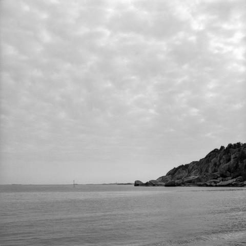 Clifs stretching into the sea.I stand visible in the distance on the horizon line. Slightly wavy seas, speckled clouds in the sky.