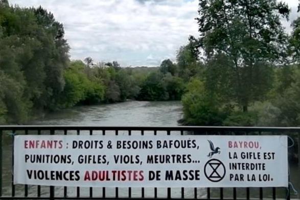 Banderole déroulée sur un pont du Gave de Pau, est écrit : ENFANTS : DROITS&BESOINS BAFOUES, PUNITION, GIFLES, VIOLS, MEURTRES... VIOLENCES ADULTISTES DE MASSE. / Bayrou, la gifle est interdite par la loi.
