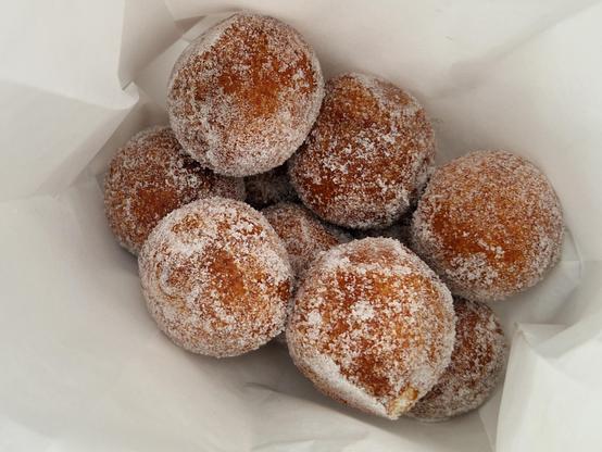Round doughnuts covered in sugar in a paper bag.