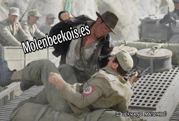 Scène tirée d'un film d'Indiana Jones dans laquelle le personnage principal, habillé en aventurier avec un chapeau, donne un coup de poing à un soldat nazi. Le mot "Molenbeekois.es" est écrit en lettres noires sur fond blanc par-dessus Indiana Jones. Le logo "© Lefranc Matombé" apparaît en bas à droite de l’image.