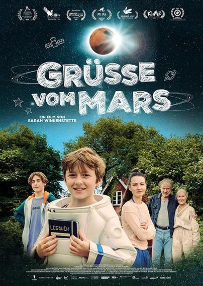 Das Bild zeigt das offizielle Filmplakat zum Kinder- und Familienfilm **„Grüße vom Mars“**, inszeniert von **Sarah Winkenstette**.

Im Zentrum des Plakats steht ein lächelnder Junge in einem weißen Raumanzug, der ein „Logbuch“ in den Händen hält – offenbar die Hauptfigur. Um ihn herum sieht man weitere Familienmitglieder oder enge Bezugspersonen, darunter Jugendliche und Erwachsene, die ihn freundlich oder liebevoll anschauen. Die Kulisse ist ein ländlicher, grüner Garten mit Bäumen und einem kleinen roten Häuschen – eine idyllische, bodenständige Szenerie im Kontrast zum Weltraumthema des Titels.

Der obere Bereich des Posters zeigt eine Illustration des Planeten **Mars**, der von Sternen, einem Satelliten und gezeichneten Raumfahrtsymbolen umgeben ist. Diese sind kindlich-skizzenhaft gehalten und verleihen dem Plakat eine verspielte, fantasievolle Note.

In großen weißen Buchstaben steht der Titel **„GRÜSSE VOM MARS“** im Mittelpunkt.
Darunter:
**„Ein Film von Sarah Winkenstette“**

Am oberen Rand befinden sich zahlreiche Logos und Lorbeerkränze von Festivals und Filmpreisen – ein Hinweis auf die positive Resonanz, die der Film bereits erhalten hat.

Der Gesamteindruck des Plakats vermittelt einen warmherzigen, optimistischen Film, vermutlich mit Themen wie kindlicher Fantasie, Familie, Zusammenhalt und vielleicht der Sehnsucht nach anderen Welten – real oder metaphorisch.

Möchtest du eine kurze Inhaltsangabe oder Hintergrundinfos zur Regisseurin?
