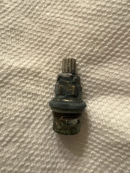 The cartridge from a bathroom faucet that is covered in corrosion and ick.