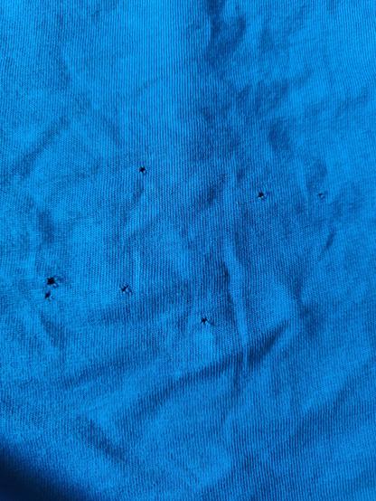 Stukje van de onderkant van een blauw shirt met 7 gaatjes er in.