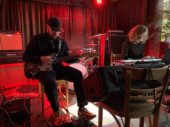Guitar player and electronic musician performing in red lighting