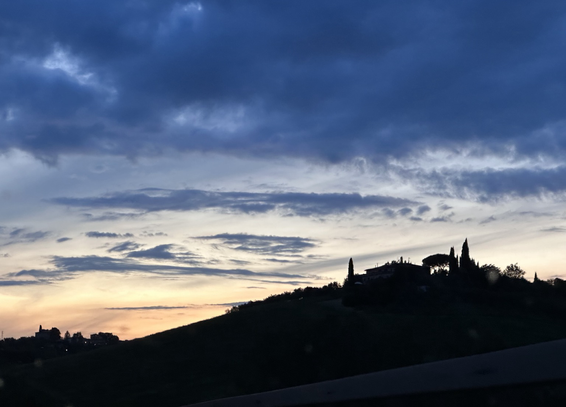 Dark outline of hill with farm on top against a sky with orange colors and dark clouds