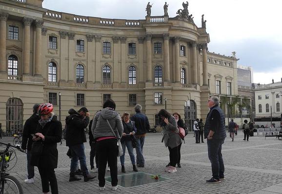 Passanten betrachten die in den Boden eingelassene Gedenktafel an die Bücherverbrennung am 10. Mai 1933 auf dem Berliner Bebelplatz, auf der eine Rose liegt. 