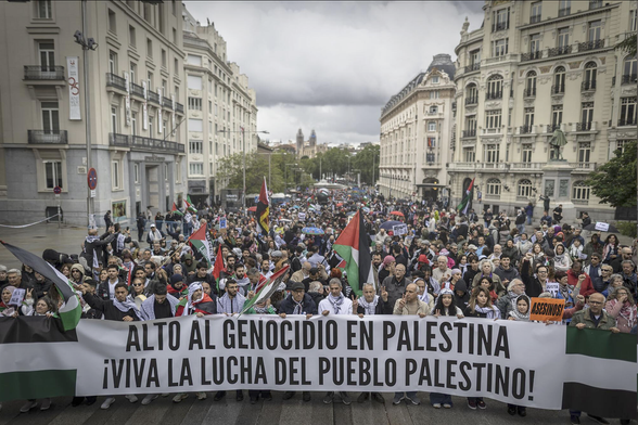 Pancarta principal de la manifestación del 10 de mayo de 2025 "Muevete por Palestina" en Madrid.

Una gran multitud de manifestantes se congrega en una calle ancha entre edificios altos de una ciudad.  La multitud lleva pancartas y banderas palestinas, y una gran pancarta en primer plano dice "Alto al Genocidio en Palestina ¡Viva la Lucha del Pueblo Palestino!". La atmósfera parece tensa pero determinada. El cielo está nublado.