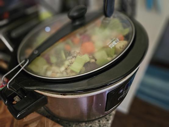 Picture of a slow cooker packed full with roast, carrots, onions, celery, garlic, red potatoes. 