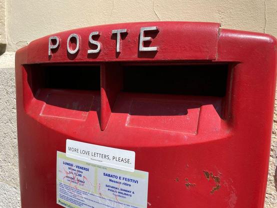 A close-up of a red Italian mailbox with the word "POSTE" and a small sticker reading "More love letters, please."