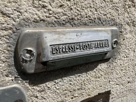 A vintage metal mail slot labeled "Espressi - Posta Aerea" embedded in a stone wall.