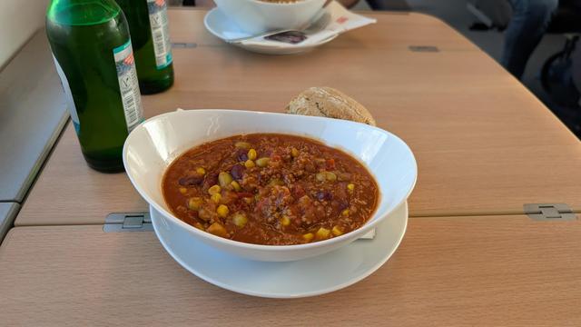Chili sin Carne vom DB-Bordbistro im Teller mit Brötchen auf einem Holztisch