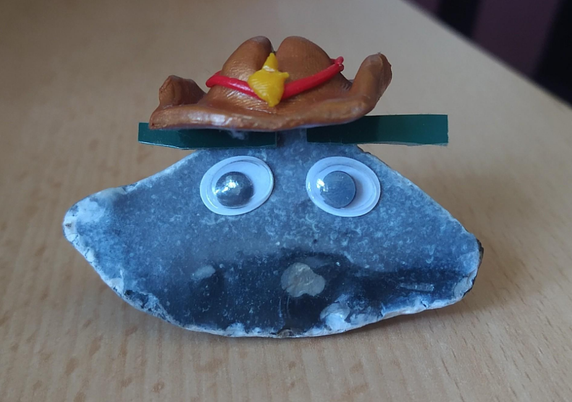 A pet rock with googly eyes, eyebrows and a polymer clay cowboy hat.