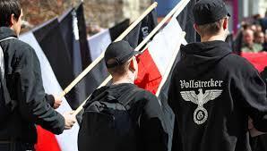 Photo d’une manifestation dans les rues de Paris, avec des participants tenant des drapeaux français et des symboles identitaires d’extrême droite (croix celtique, slogans catholiques). Le visuel contient un message en surimpression dénonçant l’intolérance religieuse envers les libres penseurs, les rationalistes et les athées.
