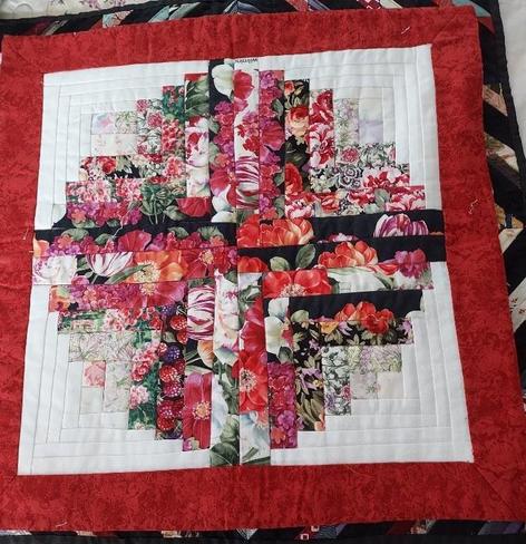 a quilt, it has a thick red border with a white square  in the center, in the square is a large floral cross design 