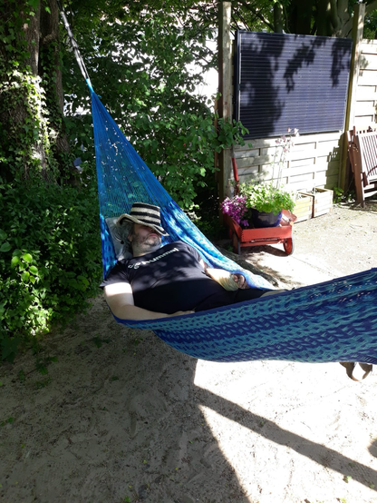 Mann mit Hut tief im Gesicht, entspannt in einer Hängematte. Im Hintergrund ein PV-Modul