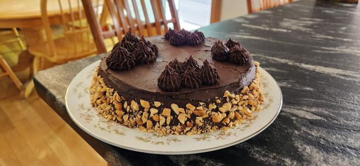 Chocolate frosted cake on a plate on my kitchen counter. Crushed peanuts are along the edge.