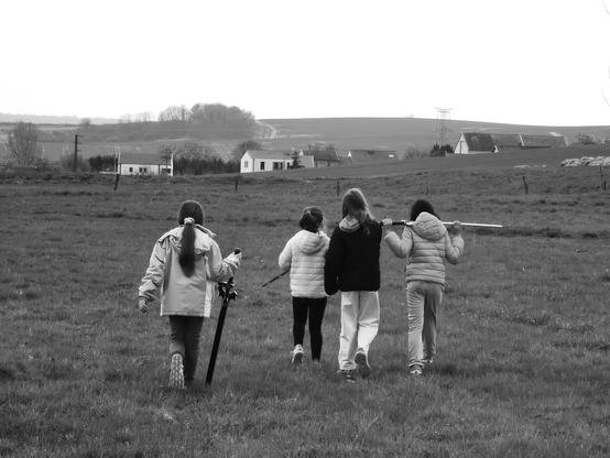 Quatre grandes enfants traversent une prairie en direction d'un village, avec des épées de cosplay, comme revenant d'une quête éreintante