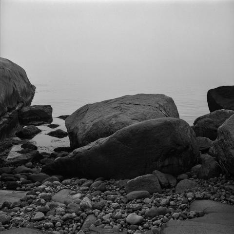 Rocky coastal landscape with rocks of all sizes from small to huge. The sea in the background, almost completely obscured by fog.