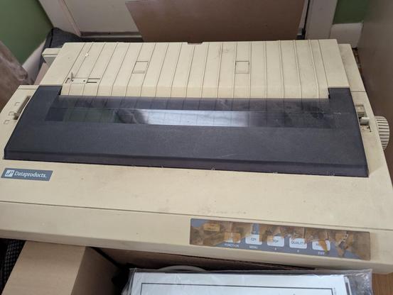 A photograph of a Dataproducts wide-format dot matrix printer.  It's dusty, and the plastic protective film over the buttons on the front has turned brown and cracked and flaked away.