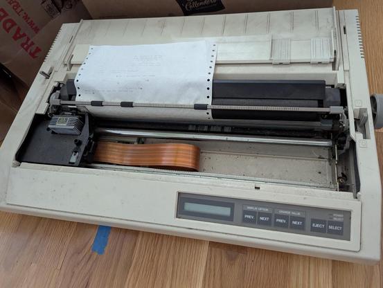 A photograph of another wide-format dot matrix printer, also dusty and full of debris, but looking to be in better condition.  This one has no badge on the front, but the type plate on the back shows that it's a Toshiba P341SL.