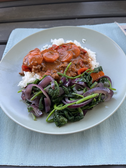 Ein Teller mit Reis, einem Curry mit Möhren und Paprika, dazu Spinat mit Zwiebeln.