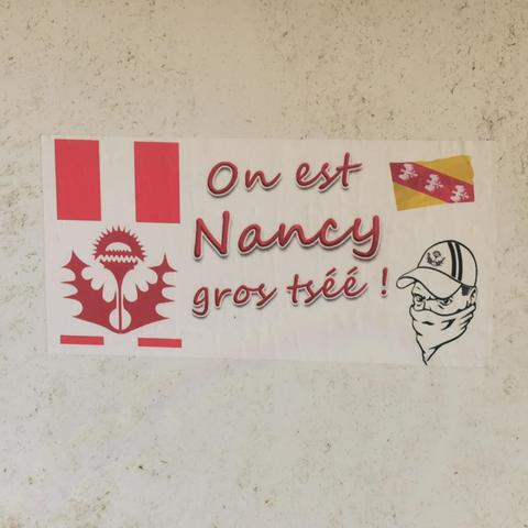 Collage sur un mur dans la région de Nancy, il représente les symboles de la Lorraine (chardon et drapeaux) aux couleurs du club de foot local, l'ASNL. Un supporter est également représenté avec une casquette et le visage caché par un foulard, seuls ses yeux sont visibles