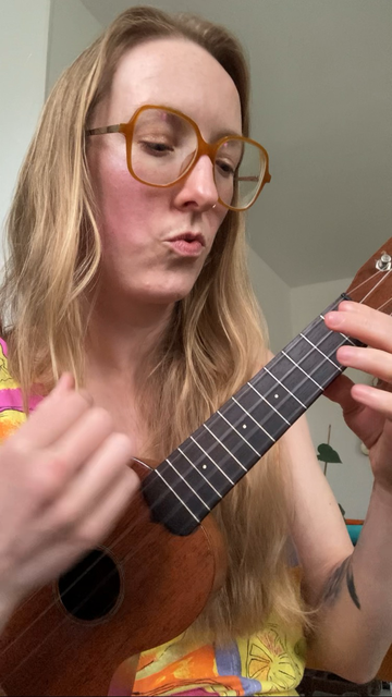 Sage, in a colorful sun dress, plays ukulele and sings 